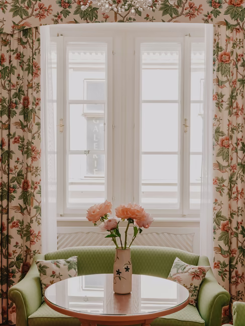 Sitzecke aus kleiner grüner Couch und rundem Holztisch mit einer Vase voller rosaroten Pfingstrosen