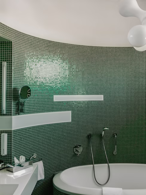 Badezimmer mit Badewanne, Waschbecken mit großem Spiegel und vielen kleinen grünen Fließen