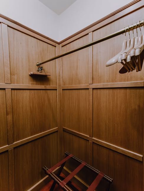 Begehbarer Schrankraum aus Holz mit Kleiderbügeln und kleinem Hocker