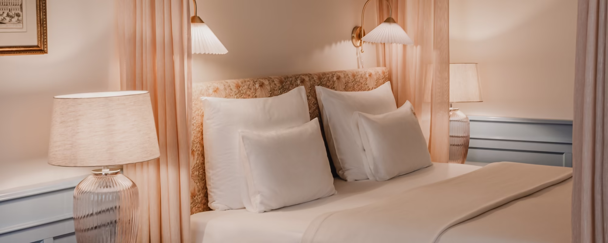 Das Bett mit seitlich angebrachten Vorhängen und einem Nachttisch.
