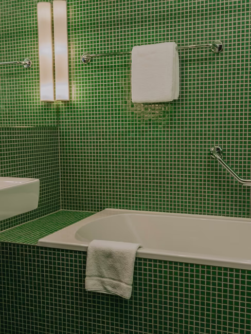 Badezimmer mit kleinen grünen Fließen mit Badewanne, Waschbecken und Handtüchern
