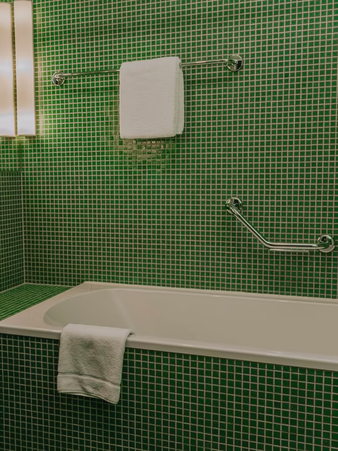 Badezimmer mit kleinen grünen Fließen mit Badewanne, Waschbecken und Handtüchern