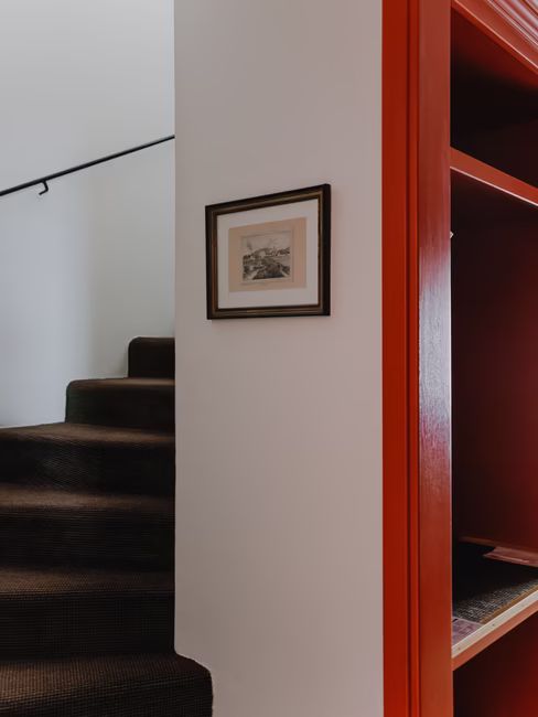 Ein Eingangsbereich mit einem roten Schrank und einer nach oben führenden Stiege.
