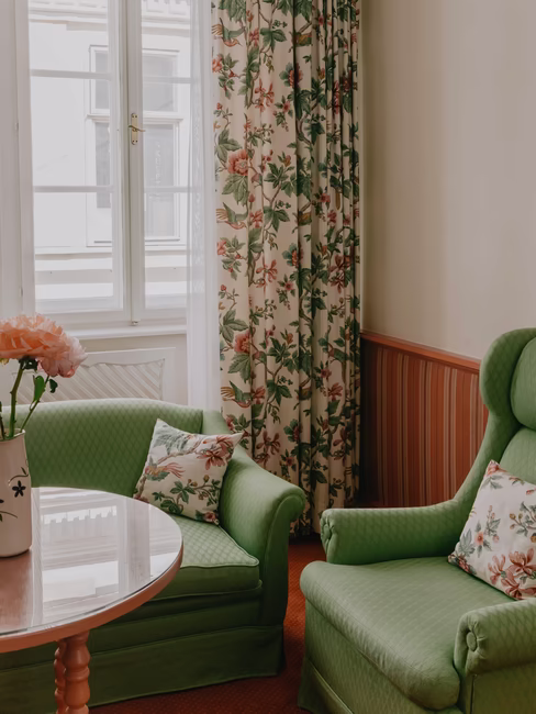 Sitzecke mit zwei großen grünen Stühlen mit Polstern und großem Fenster inkl. Gardinen mit Blumen