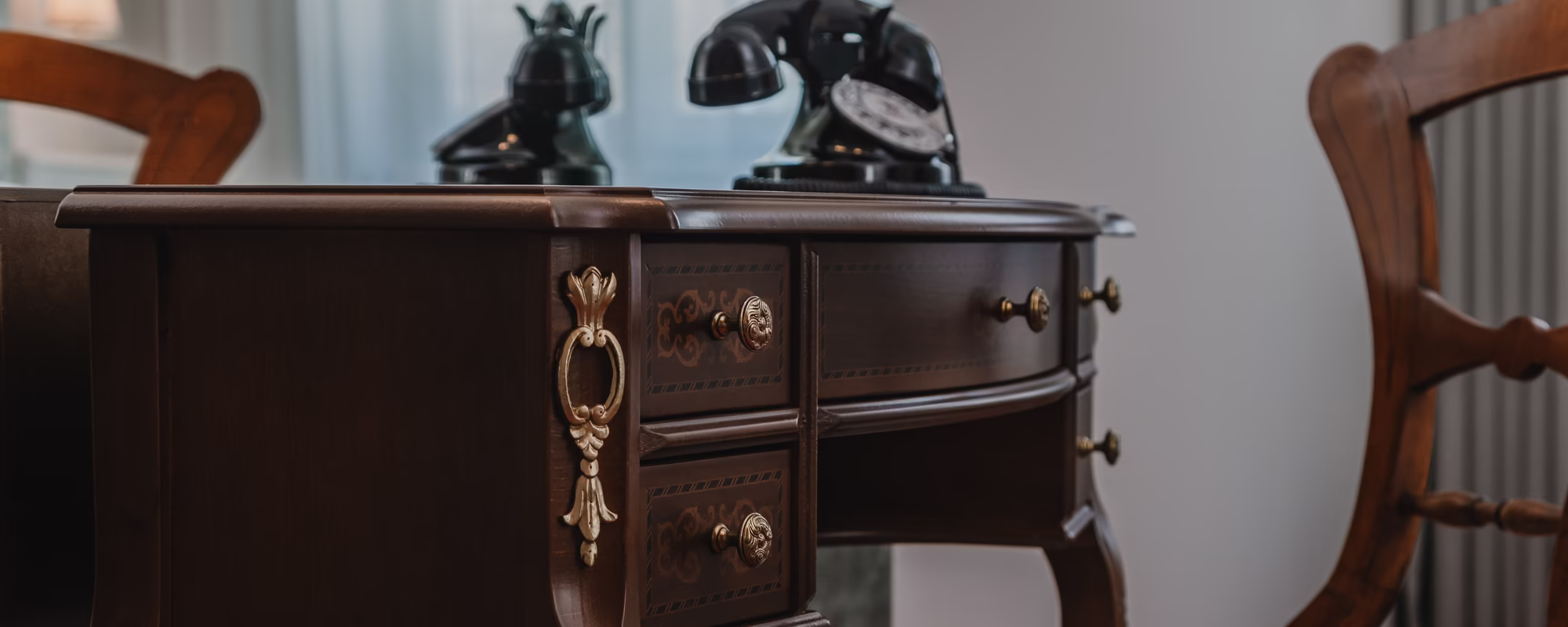 Alter Schreibtisch mit historischem Telefon und gepolstertem Holzstuhl in klassischem Ambiente