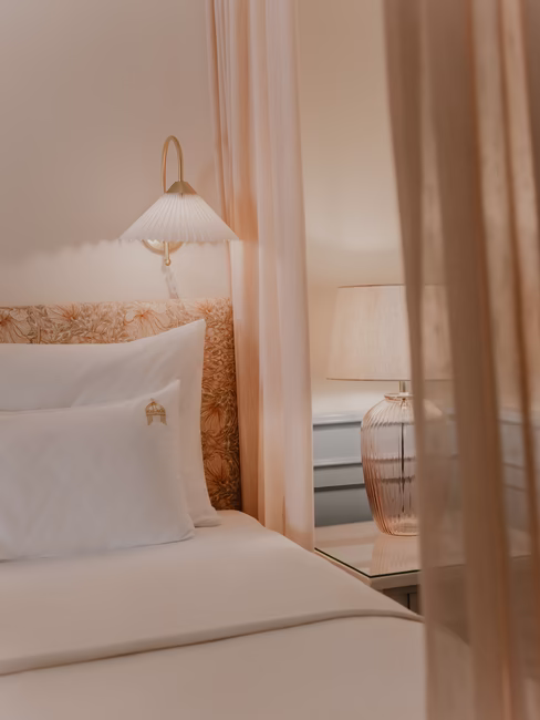 Ein Teil des Bettes mit dem dazugehörigen Nachttisch und einer daraufstehenden Lampe.
